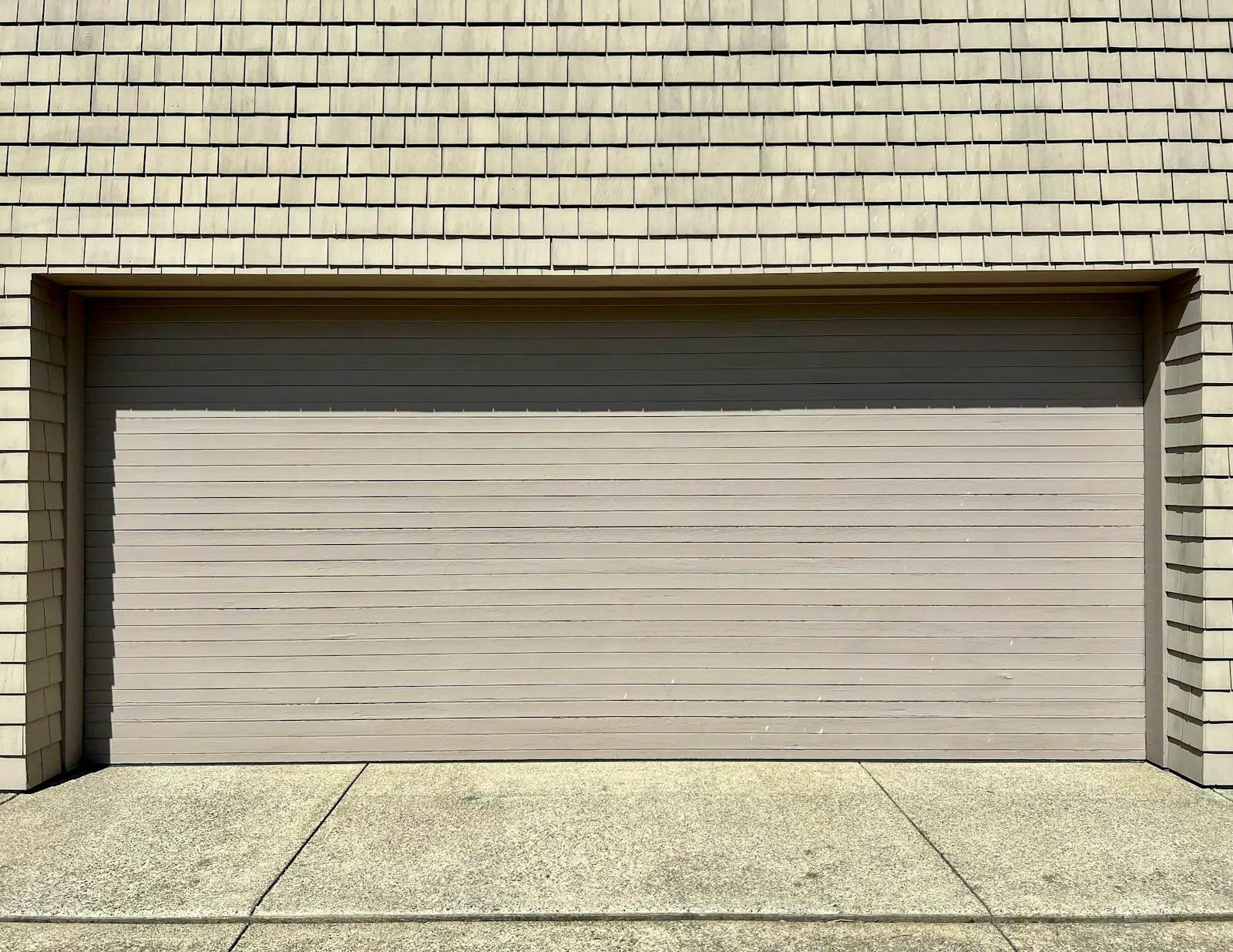 A complete neutral garage door with fine horizontal panels, framed by shingle siding.